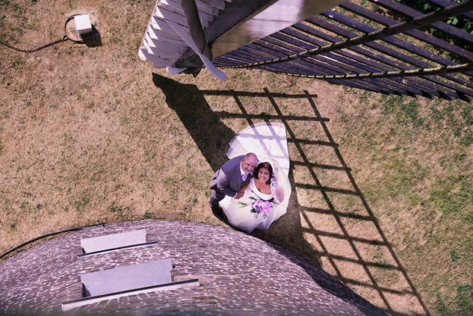 Trouwfotograaf uit Roermond in Limburg maakt foto vanuit de molen van Maasbracht van een bruidspaar bij een wiek van de molen. Speciale en aparte fotografie van een trouwdag in binnen en buitenland.