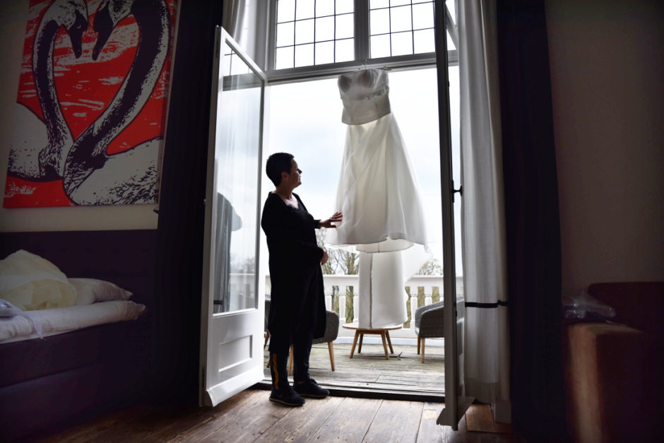Bruid kijkt naar haar trouwjurk in de kamer op landgoed Rhederoord tijdens de voorbereidingen van haar bruiloft.