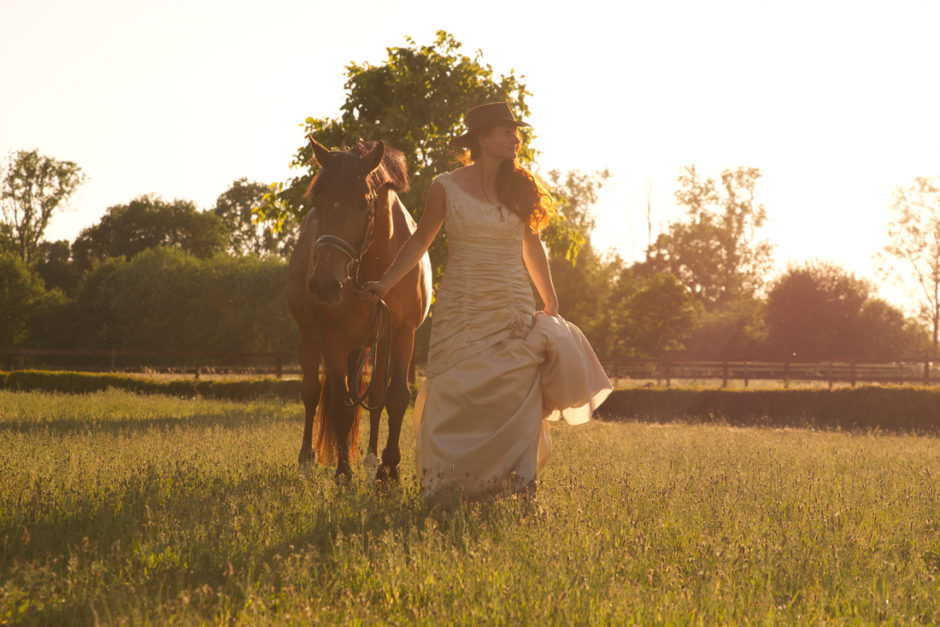 De bruid loopt met haar paard aan de hand door de wei tijdens de zonsondergang.
