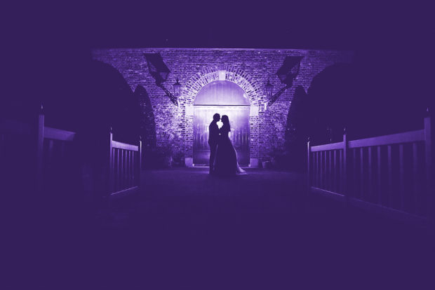 Bijzondere trouwfoto, een silhouet van het bruidspaar en paars flitslicht maken dit een hele bijzondere foto.