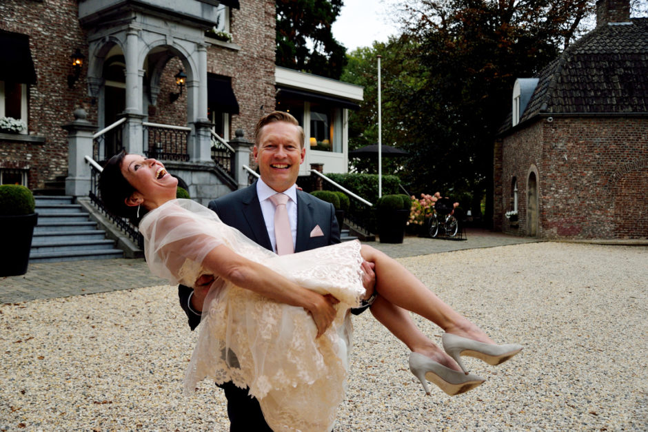 Bruidegom tilt bruid op, zodat ze met haar dure hakschoenen niet over het grind hoeft te lopen. In Limburg.