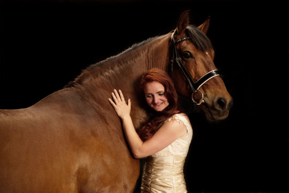 Een paard en zijn bazin portret met donkere achtergrond op stal in Limburg.
