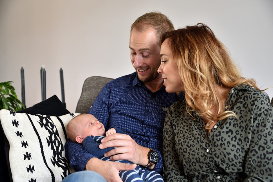 Ouders met baby op de bank in hun eigen woonkamer in Roermond tijdens een lifestyle baby fotosessie. Mooi kado voor babyshower.