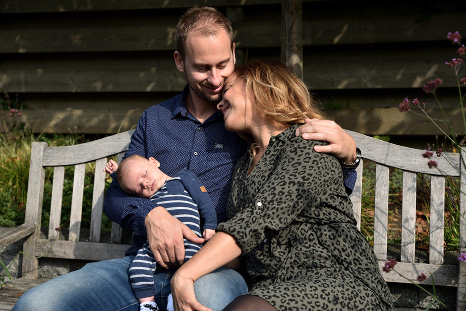 Ouders met baby op de bank in hun eigen tuin in Roermond tijdens een lifestyle baby fotosessie. Mooi kado voor babyshower.