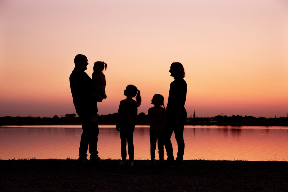 Silhouette van een gezin in Roermond. De ondergaande zon kleurt het water achter het gezin.