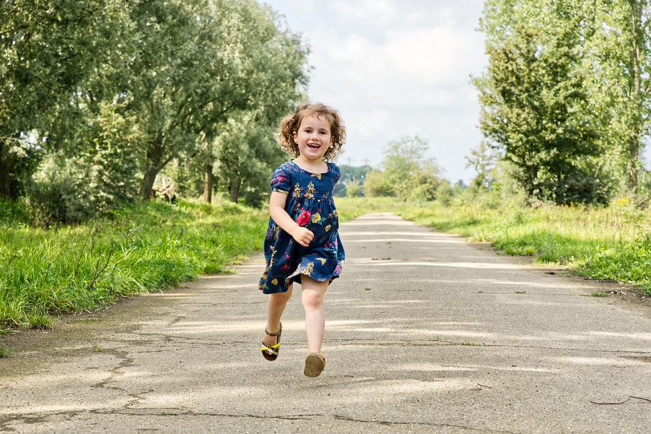 Klein Meisje rent vrolijk over het pad in de natuur in Limburg tijdens een fotoshoot met het gezin.