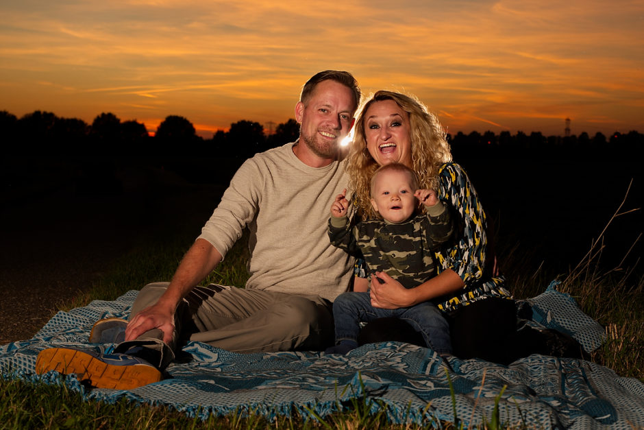 Gezinnetje met lachende baby tijdens een fotoshoot tijdens zonsondergang.