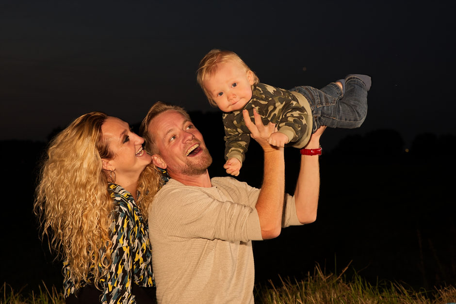 Gezinnetje, papa tilt de baby op tijdens een fotoshoot 's avonds met het gebruik van flitsers
