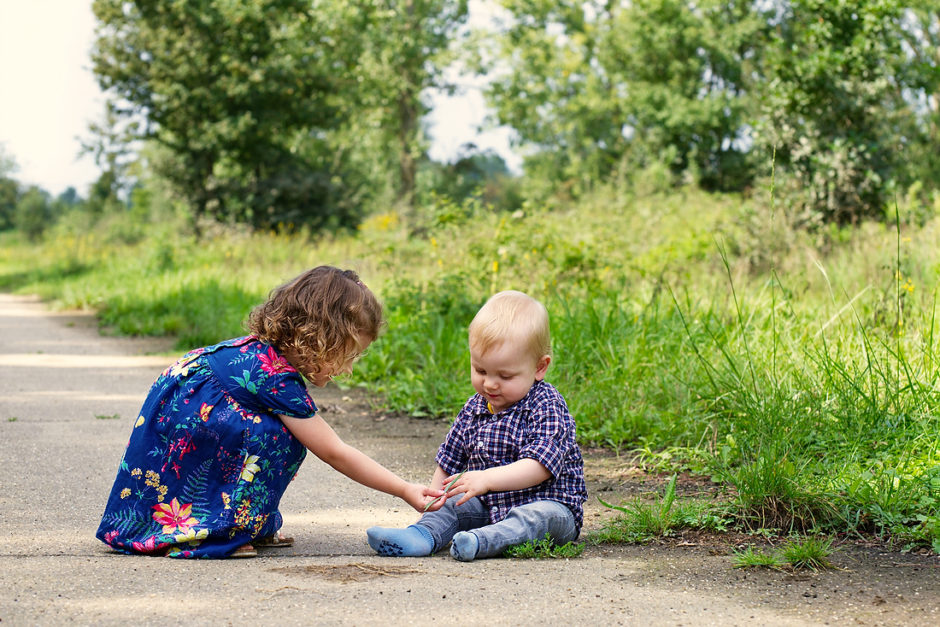 Broer en zus spelen met een blaadje op een wandelpad tijdens een ontspannen foto sessie in midden Limburg door fotograaf uit Roermond.