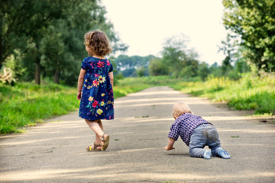 Grote zus en baby broer lopen en kruipen over het pad in de natuur in Limburg tijdens een fotoshoot met het gezin.