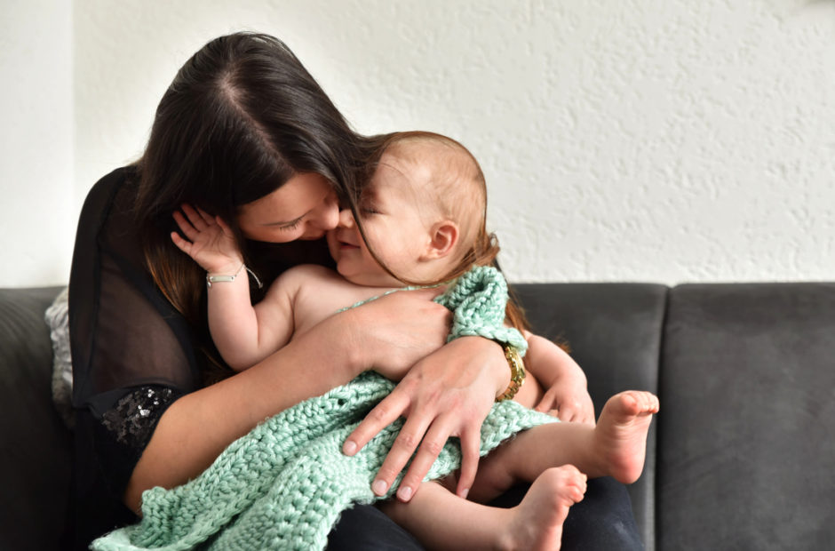 Baby fotografie in Roermond. Baby en mama knuffelen op de bank tijdens een fotoshoot thuis.