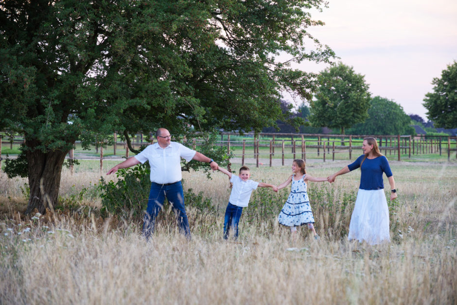 Gezin loopt hand in hand spelend naar de fotograaf toe tijdens de avond.
