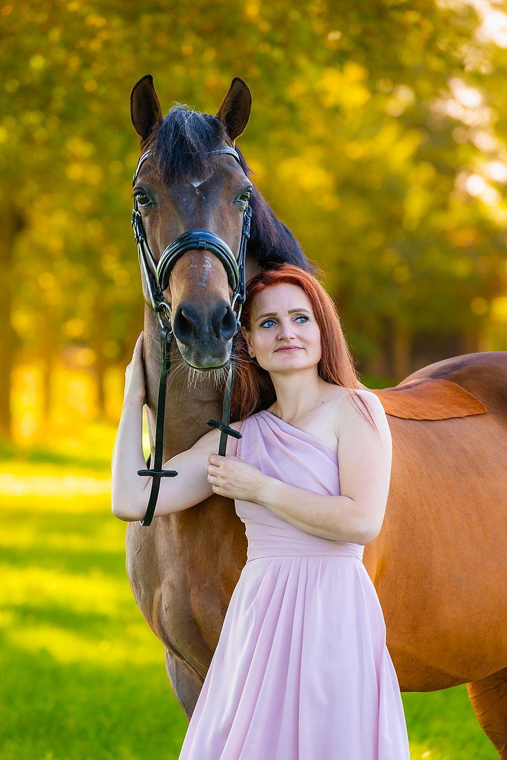 Vrouw staat in de zon met een paard in de natuur met prachtige herfst kleuren.