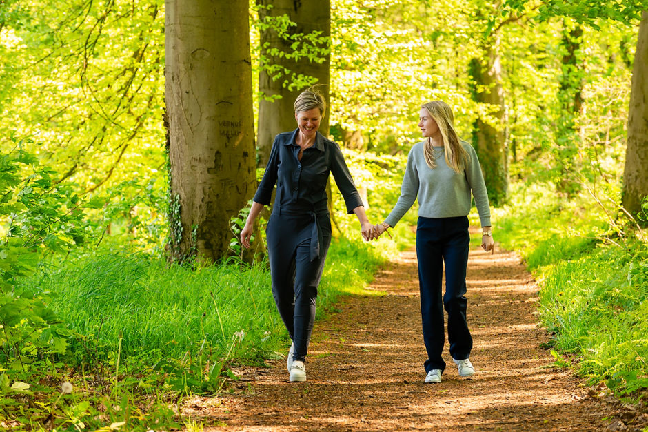 Moeder en dochter lopen hand in hand door een mooi verlicht bos in Montfort tijdens een familie fotoshoot tijdens hun weekend weg in Limburg.