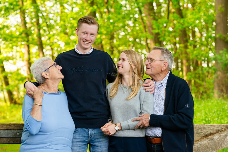 Opa en oma staan met twee kleinkinderen bij een hek in een groene omgeving. Ze hebben besloten een fotoshoot te boeken met de hele familie bij hun vakantiehuis in Montfort.