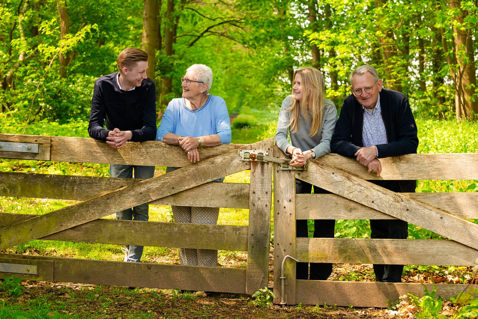 Opa en oma staan met twee kleinkinderen bij een hek in een groene omgeving. Ze hebben besloten een fotoshoot te boeken met de hele familie bij hun vakantiehuis in Montfort.