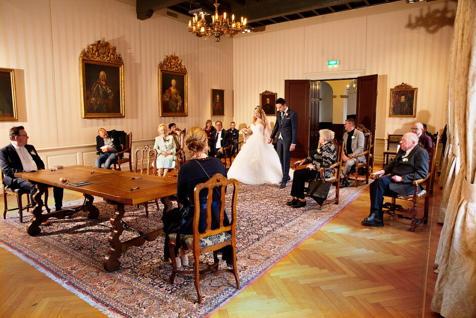 Bruidspaar loopt de trouwzaal van gemeentehuis Roermond in, terwijl de gasten naar ze kijken.