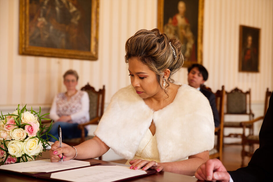 Bruid tekent de akte bij het gemeentehuis van Roermond tijdens de ceremonie.
